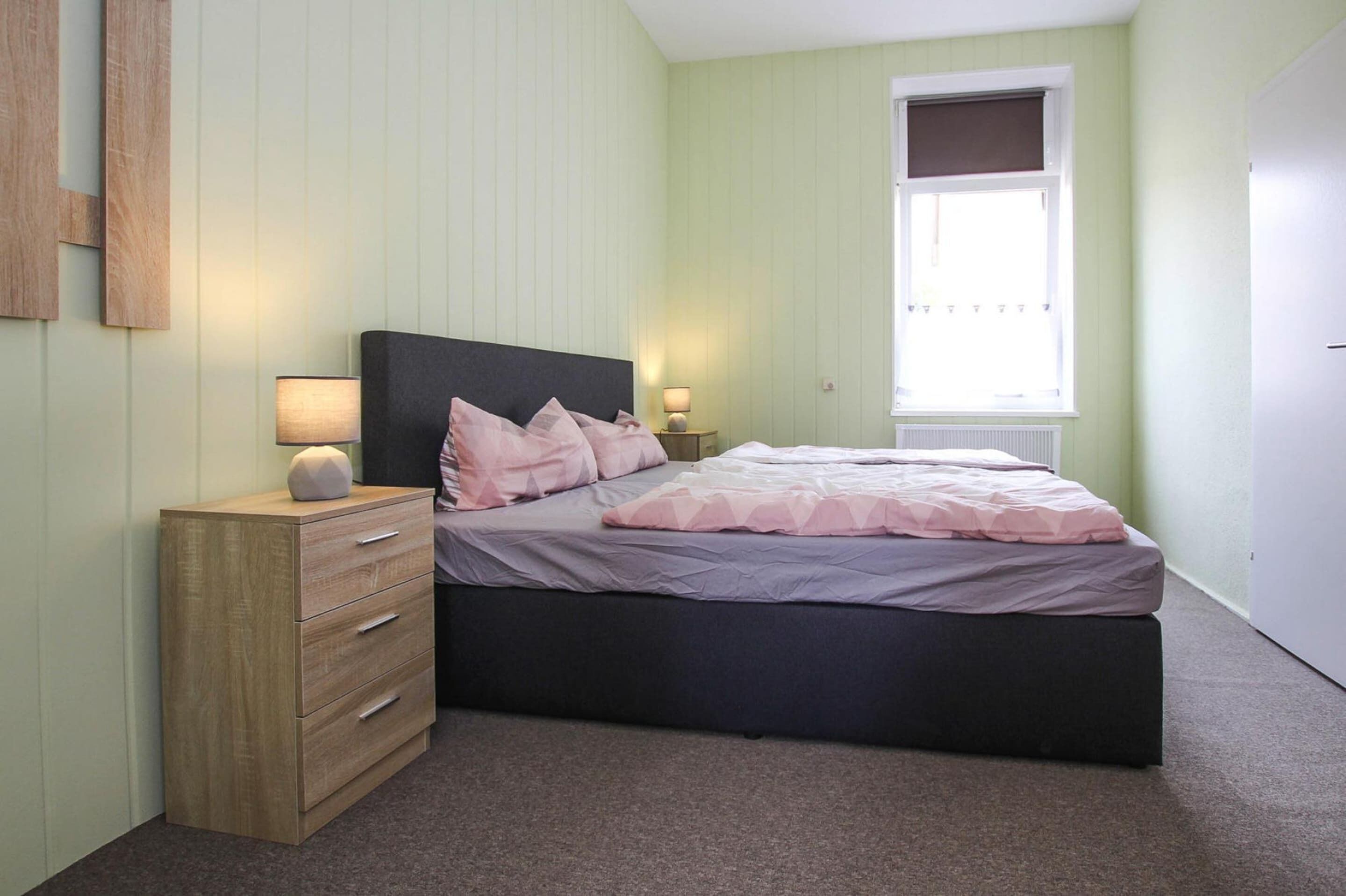 A bedroom with a bed, a nightstand, a dresser, and a window.