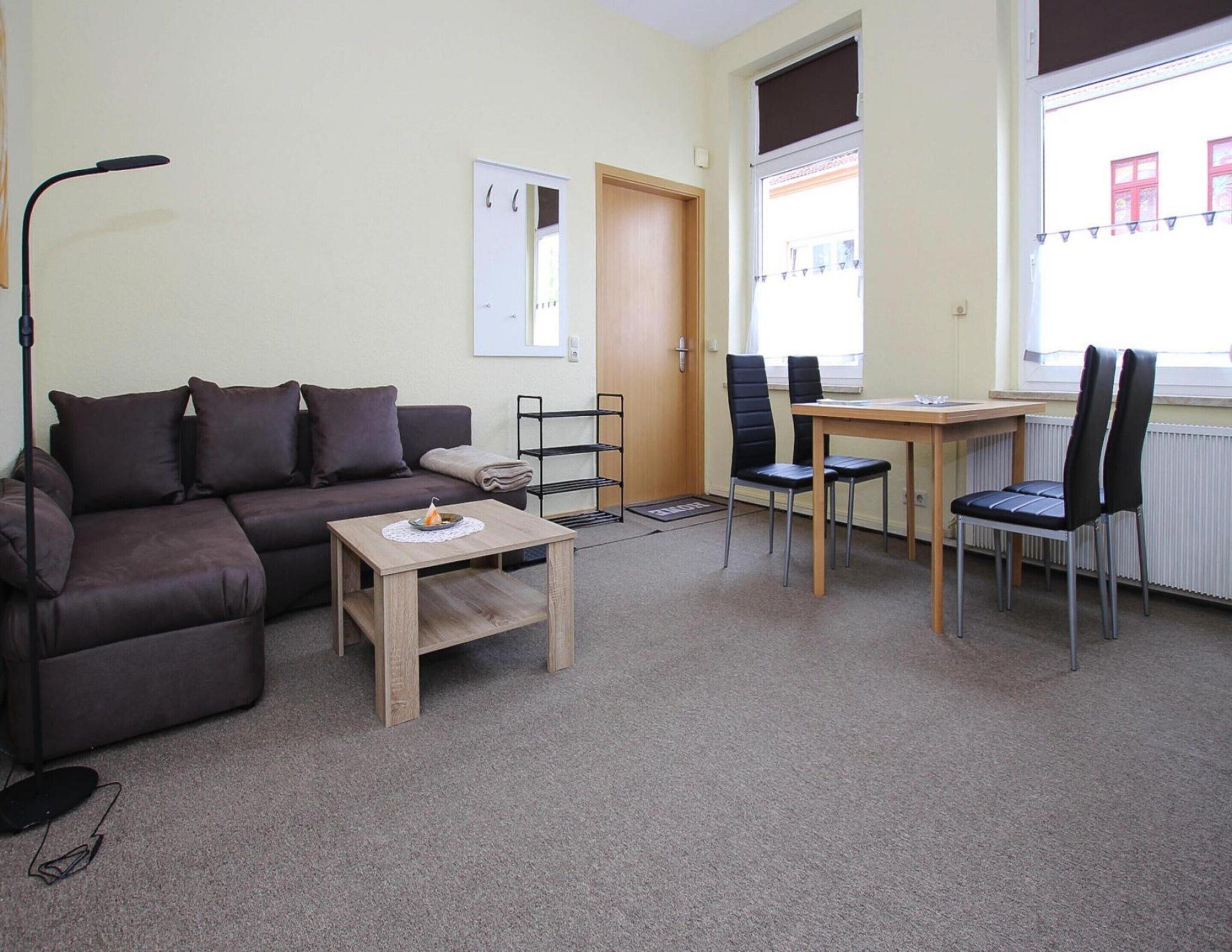 A furnished living room with a sofa, a small table, a chair, a desk, and a radiator.