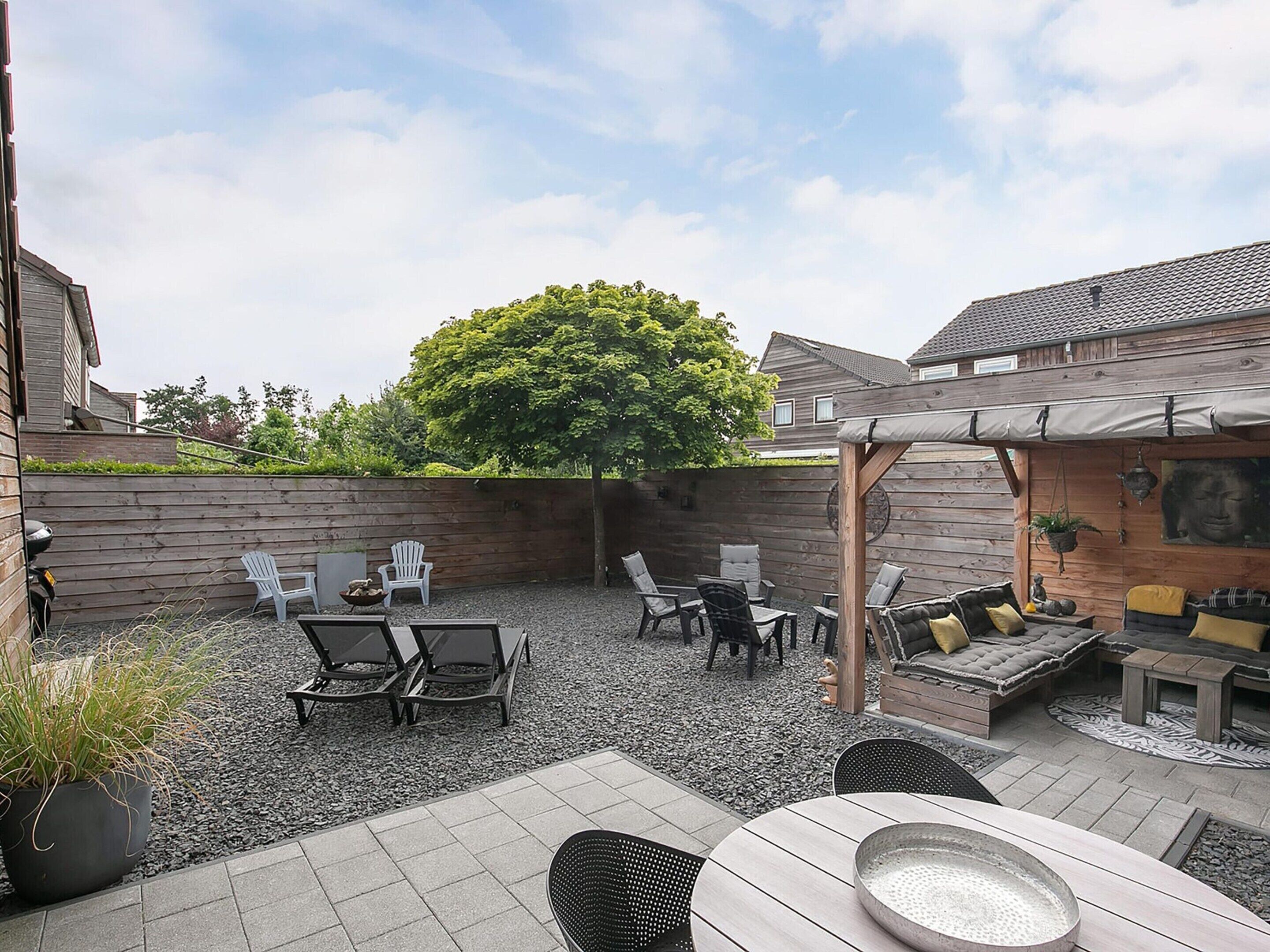 Un patio con mobiliario exterior, una pérgola y un árbol grande que ofrece sombra.