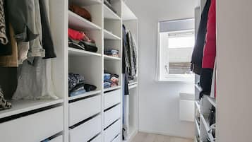 A walk-in closet with multiple shelves and drawers for storage, a window with blinds, and a wooden floor.