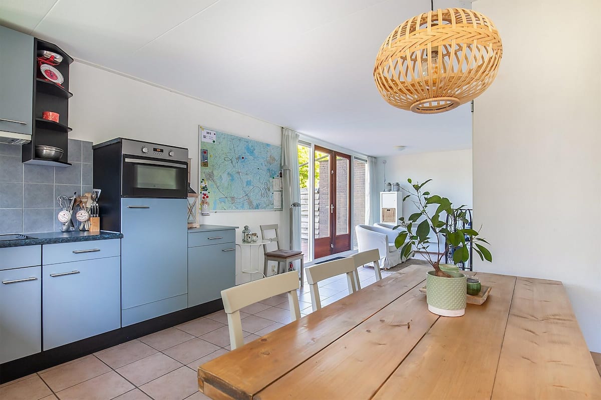 A modern kitchen with grey cabinets, a wooden dining table, and a hanging light fixture.