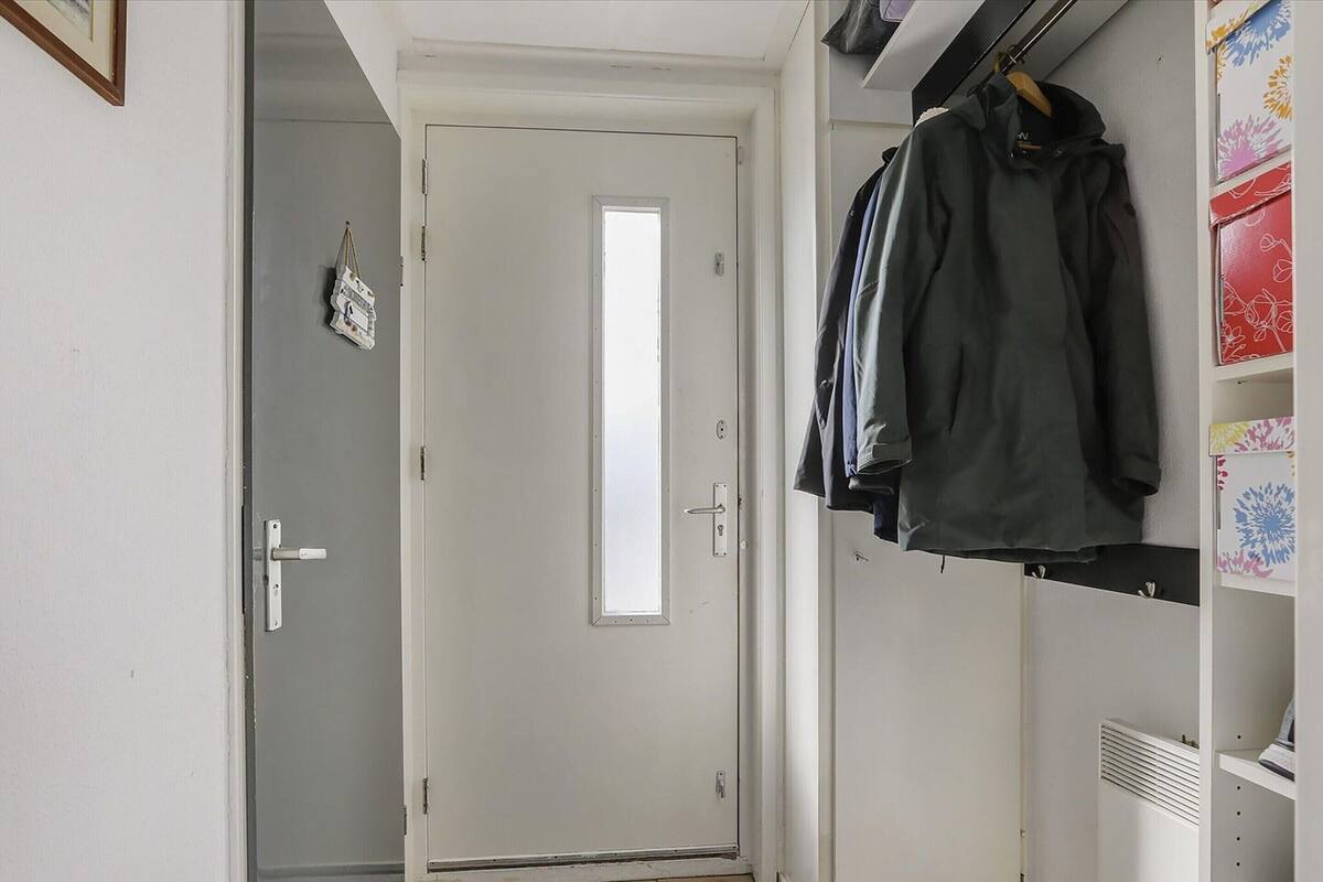 A hallway with a white door, a coat rack with several jackets, and a white shelving unit with patterned boxes.