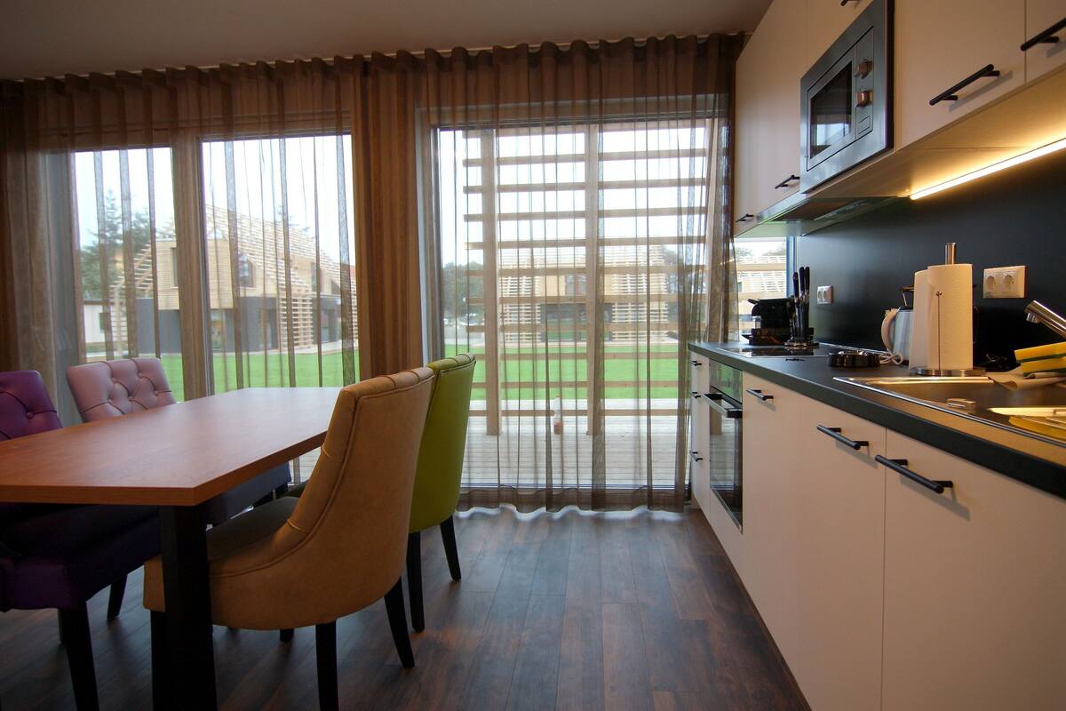 Una cucina moderna con zona pranzo, ampie finestre e vista su un prato verde.