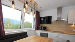 Une cuisine moderne avec une table et des chaises en bois, un four à micro-ondes et une grande fenêtre donnant sur des arbres et des montagnes.