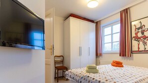 Ein Schlafzimmer mit Bett, Stuhl, Kleiderschrank, Fernseher und einem Fenster mit Vorhängen.