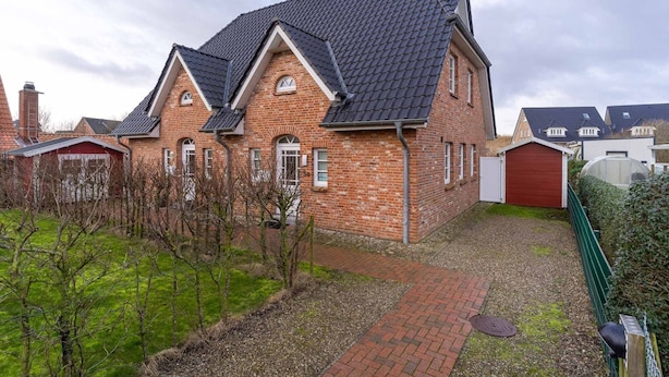 Ein Ziegelhaus mit einem dunklen Ziegeldach, einer roten Garagentür und einem gepflasterten Auffahrt.