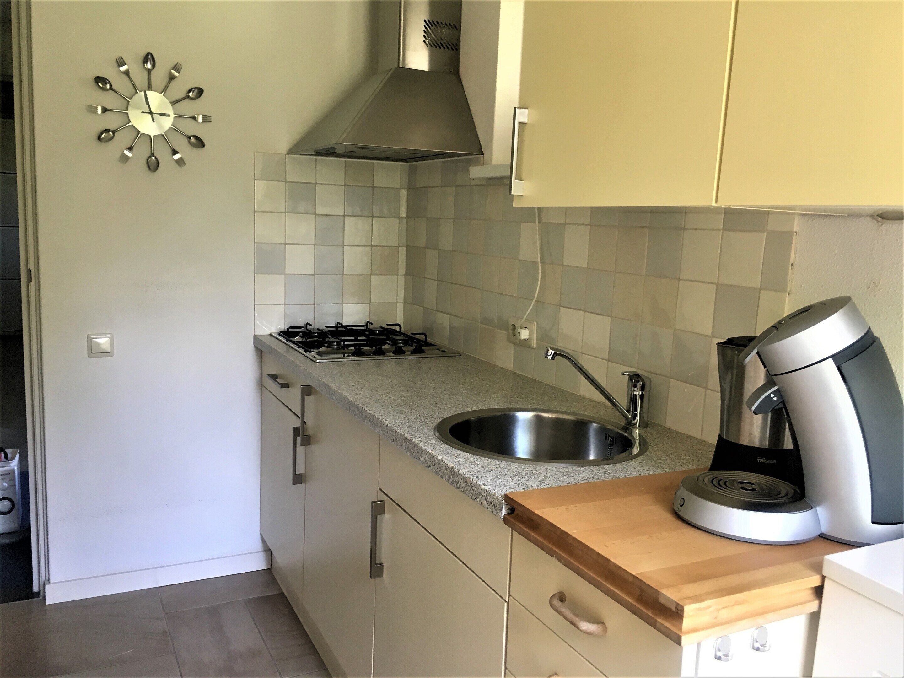 A kitchen with a gas stove, stainless steel sink, and a coffee maker.
