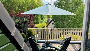 A patio with two chairs and a table, an umbrella, and a view of a white fence and greenery. - Homely Apartment in Noordwolde With Balcony (Noordwolde)