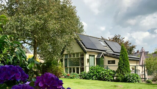 A modern house with solar panels, a well-maintained lawn, and purple flowers in the foreground. - Homely Apartment in Noordwolde With Balcony (Noordwolde)
