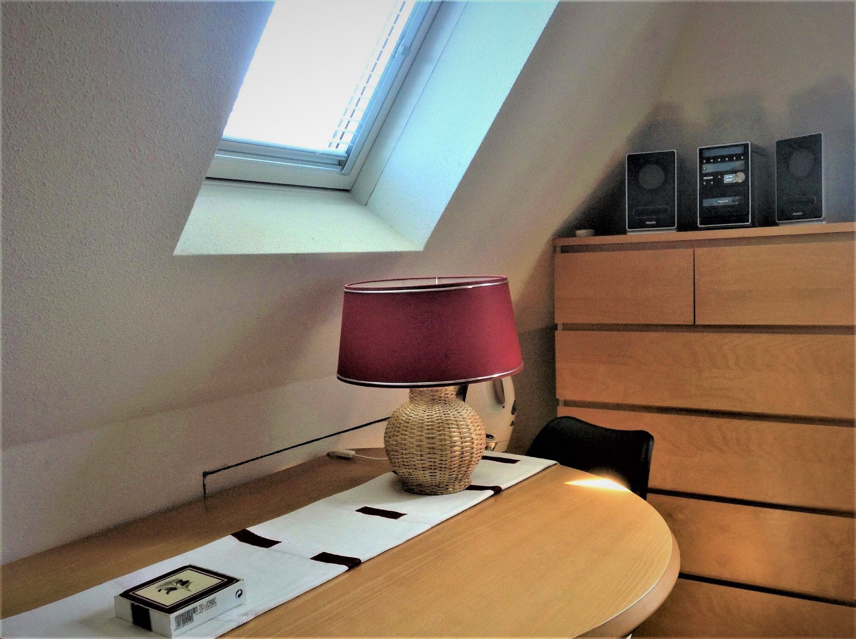 A room with a desk, a lamp, a window, and a speaker system.