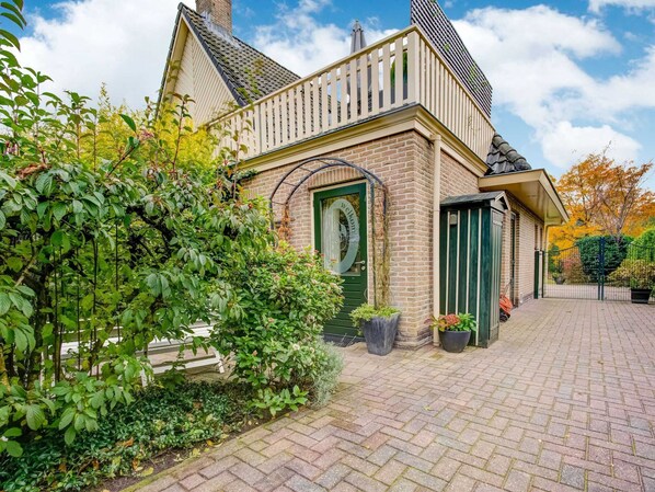 A traditional brick house with a green door, a small porch, and a brick pathway leading to the entrance.
