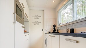 A modern kitchen with white cabinetry, a built-in oven, a coffee machine, and a window with blinds. - Homely Apartment in Noordwolde With Balcony (Noordwolde)