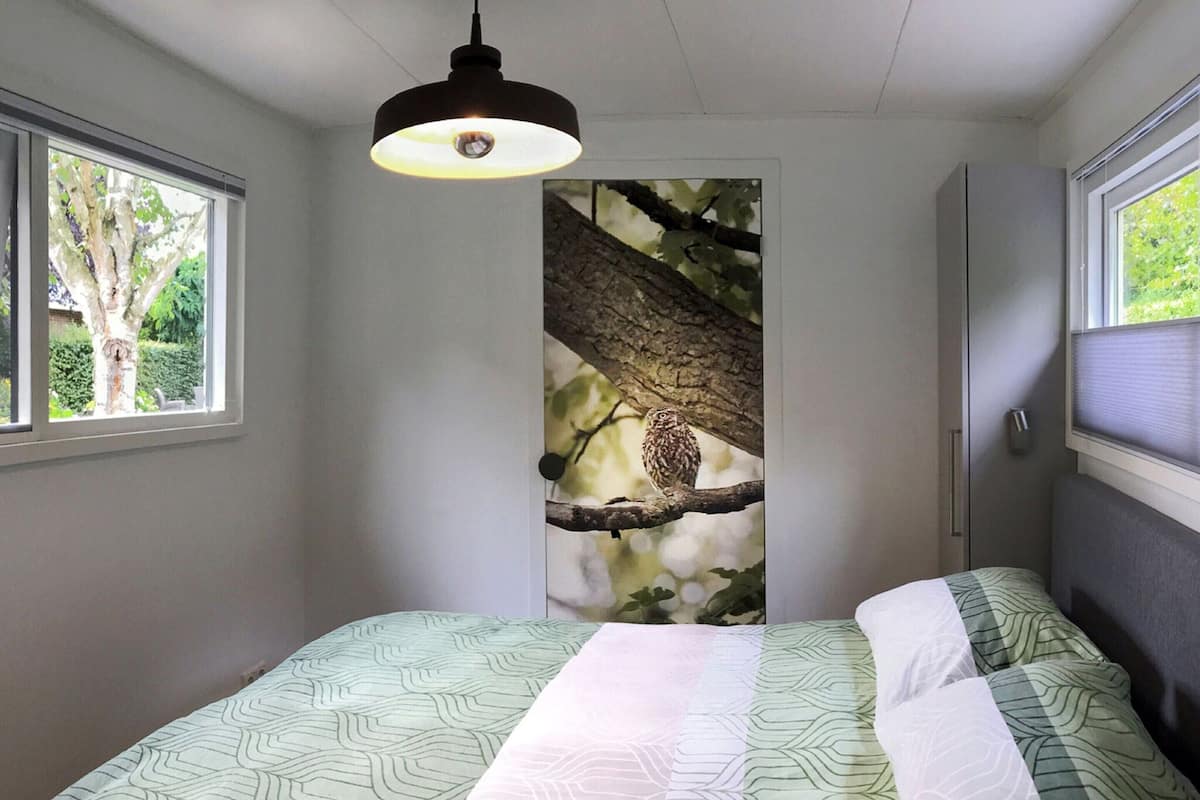 A bedroom with a bed, a window, and a wall-mounted light fixture.
