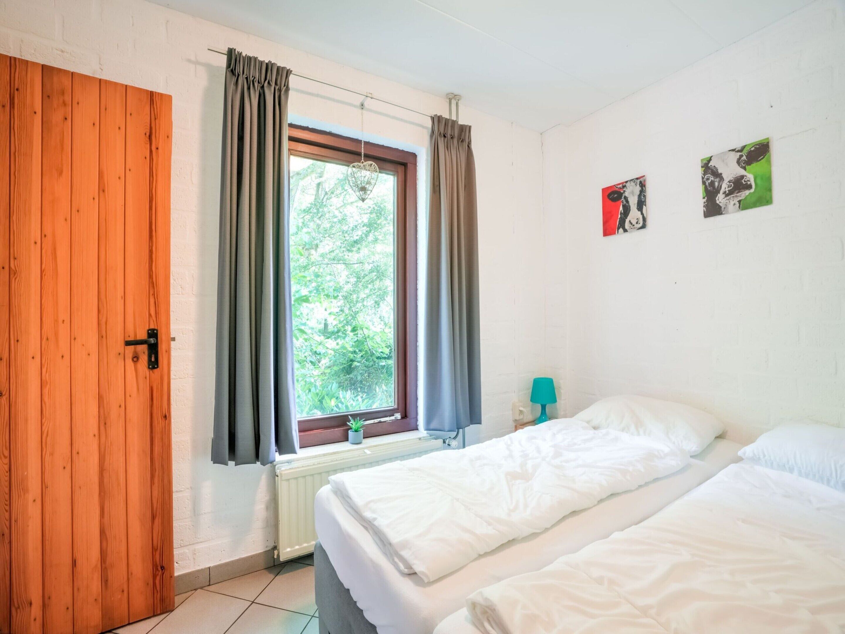 A room with two beds, a window with curtains, a radiator, and a small plant.