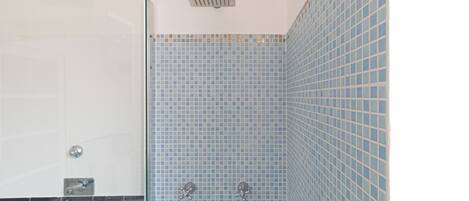 A bathroom with blue tiled walls, a shower area, and a glass partition.