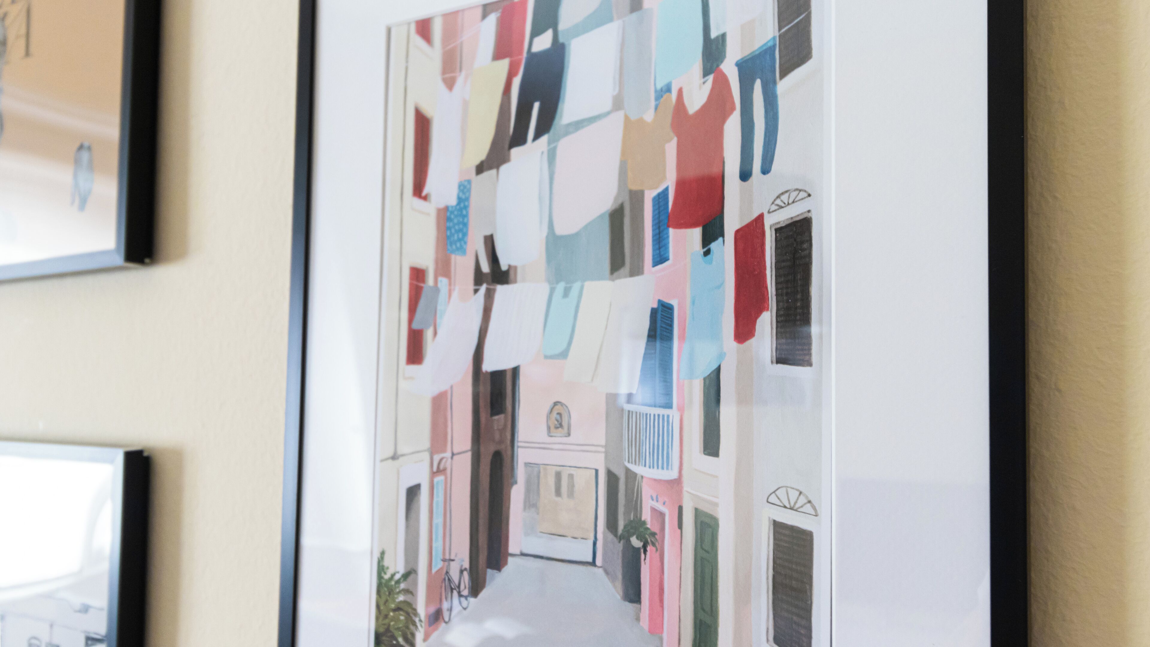 A framed artwork depicting a street scene with buildings and a bicycle.