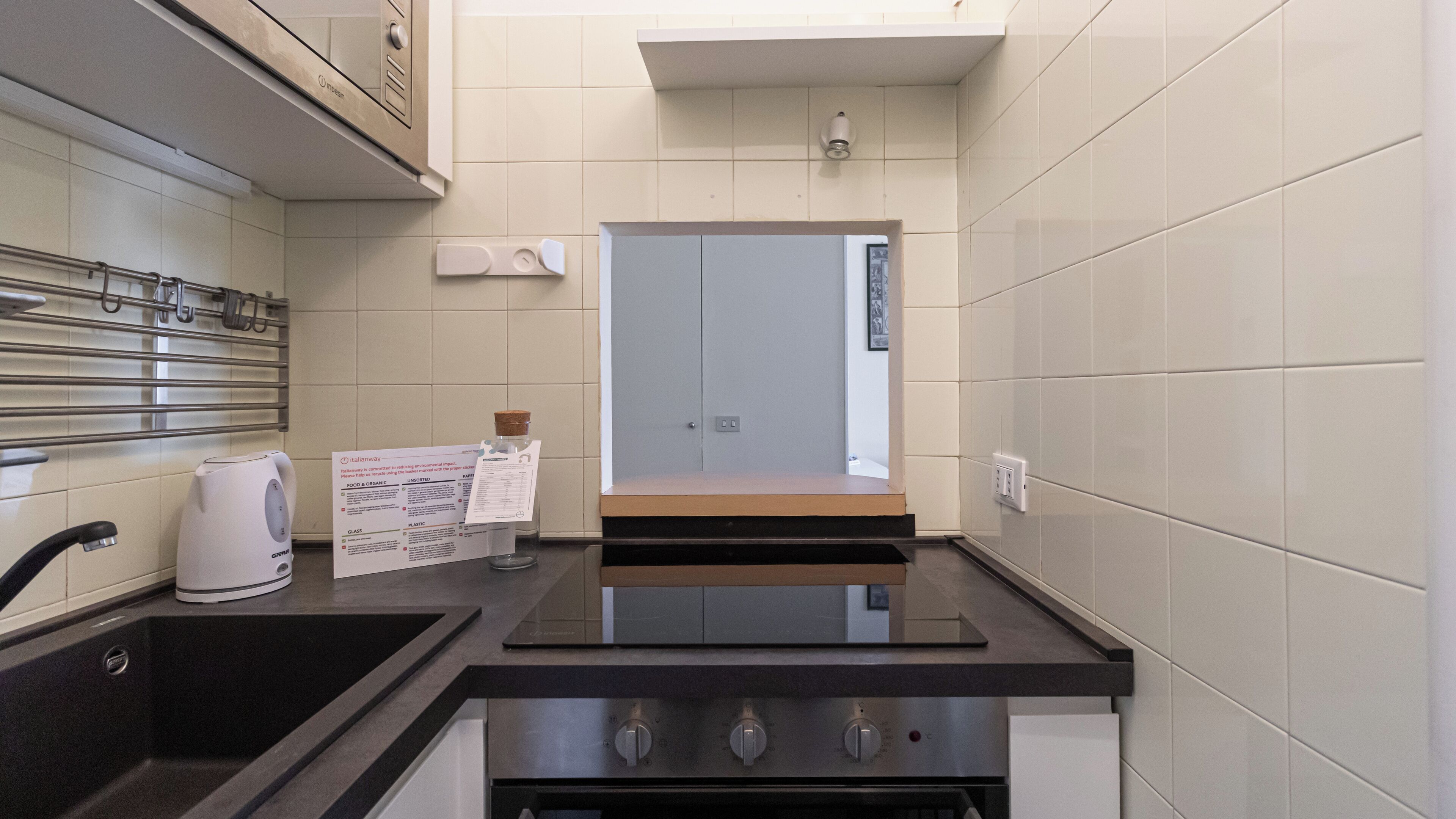 Cocina compacta con lavamanos, cafetera, campana extractora de acero inoxidable y una nota sobre el reciclaje.