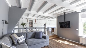 Ein modernes Wohnzimmer mit grauem Sofa, Holzboden und einem an der Wand befestigten Fernseher.