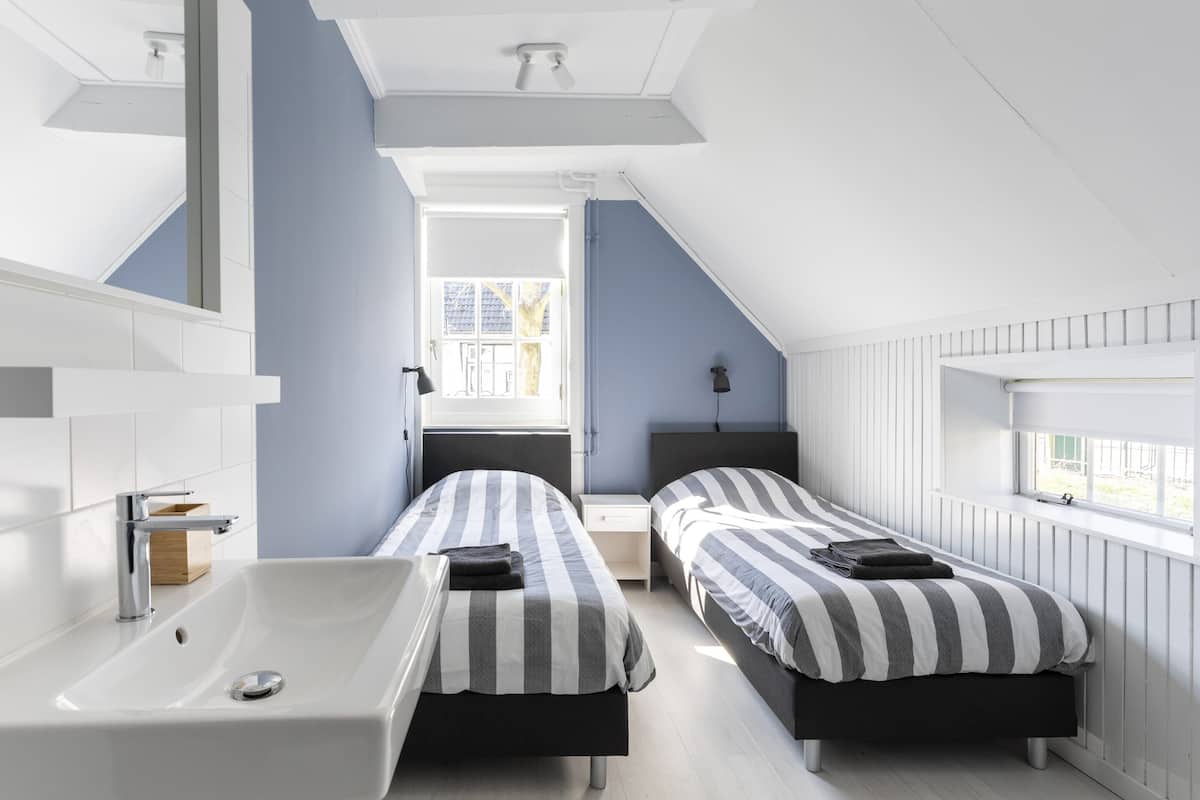 Een moderne slaapkamer met twee bedden, een groot raam en een witte wastafel.