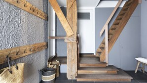 Eine Treppe mit Holzhinweisstufen und einem Holzgeländer, die zu einer Zwischenebene mit einer strukturierten Wand und einem Metallkleiderständer führt.