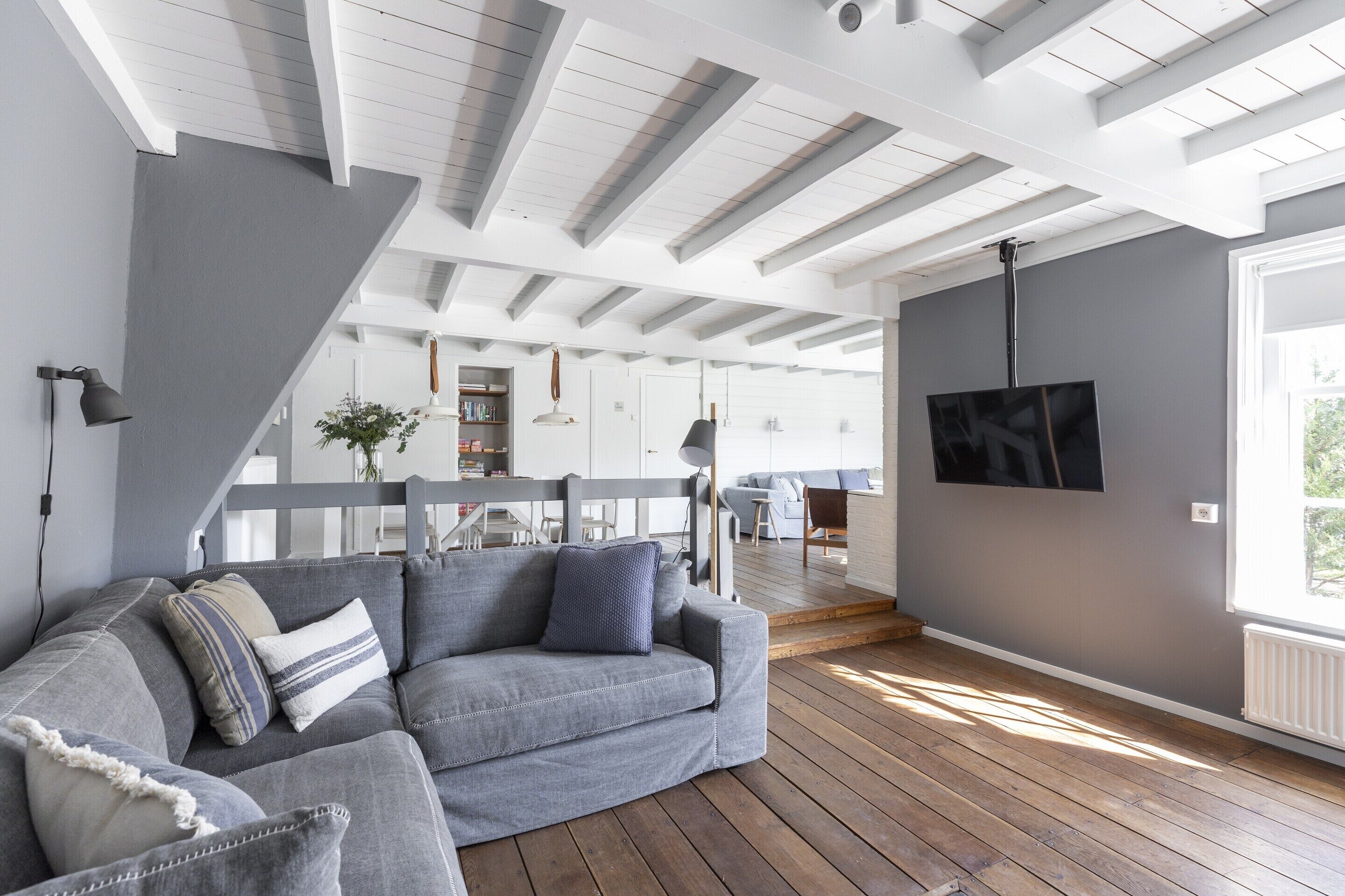 Un salon moderne avec un canapé gris, un plancher en bois et un téléviseur fixé au mur.