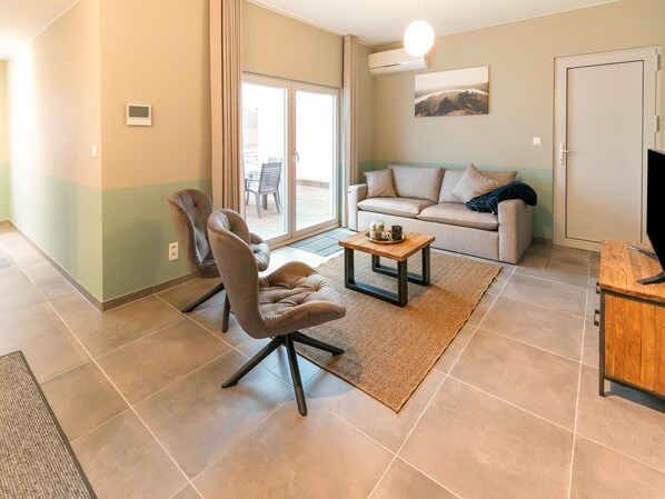 Una sala de estar con sofá, sillón, mesa de centro y televisor.