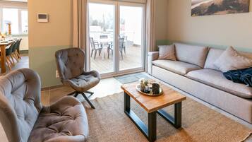 A modern living room with a sofa, two armchairs, a coffee table, and a view through a sliding glass door to an outdoor patio.