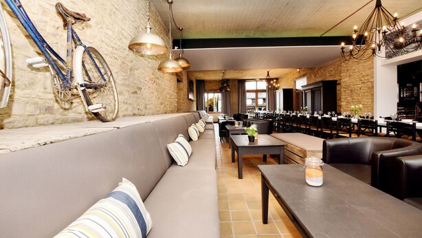 A restaurant with a long counter, cushioned seating, and a bicycle mounted on the wall. - Fancy Holiday Home in Sainte-cecile With Pool House & Indoor Pool (Florenville)