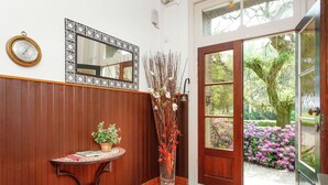 Pared de paneles de madera, una mesa redonda con una planta en maceta, un jarrón alto con ramas y una puerta que da a un jardín.