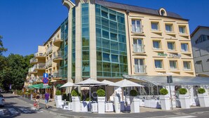 A multi-story hotel with a glass facade, outdoor seating area with umbrellas, and a sign for 'Malaquita Hotel.' - Exquisite Apartment in Miedzyzdroje With Balcony (Międzyzdroje)