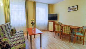 A furnished living room with a sofa, a table, a TV, and a small dining area with chairs. - Exquisite Apartment in Miedzyzdroje With Balcony (Międzyzdroje)