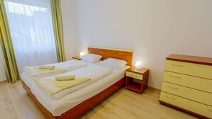 A double bed with pillows and a nightstand, a wooden dresser with drawers, and a window with curtains. - Exquisite Apartment in Miedzyzdroje With Balcony (Międzyzdroje)