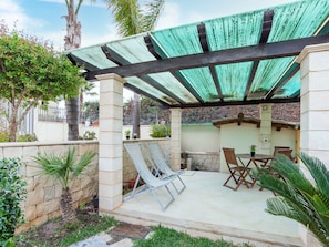Un patio couvert avec une table et des chaises, des piliers en pierre et un toit végétalisé.