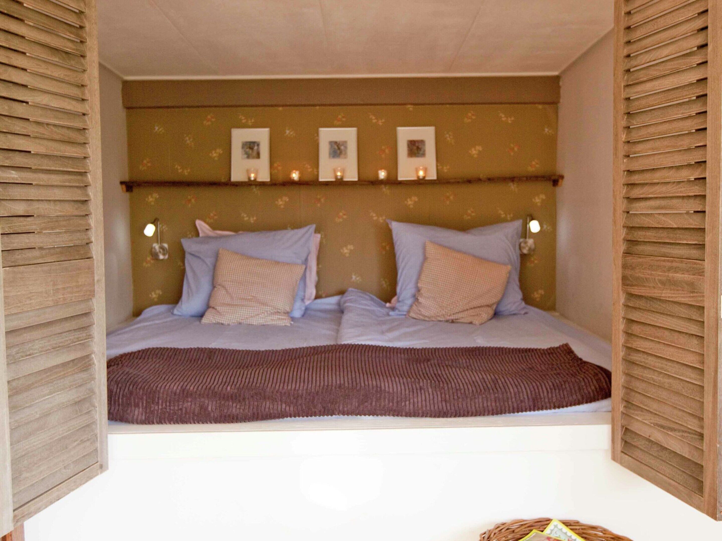 Un dormitorio acogedor con cama, dos almohadas, una manta marrón y luces fijadas a la pared.