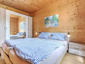A bedroom with a wooden ceiling, a bed with blue checkered bedding, a nightstand, and a wall-mounted lamp. - Detached Wooden Chalet in Liebenfels / Carinthia Near the Simonhohe ski Area (Liebenfels)