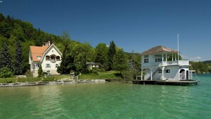 A houseboat with a balcony and a covered deck, surrounded by clear water and greenery. - Detached Wooden Chalet in Liebenfels / Carinthia Near the Simonhohe ski Area (Liebenfels)