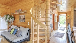 A wooden interior with a spiral staircase, a sofa with cushions, a refrigerator, and a plant. - Detached Wooden Chalet in Liebenfels / Carinthia Near the Simonhohe ski Area (Liebenfels)