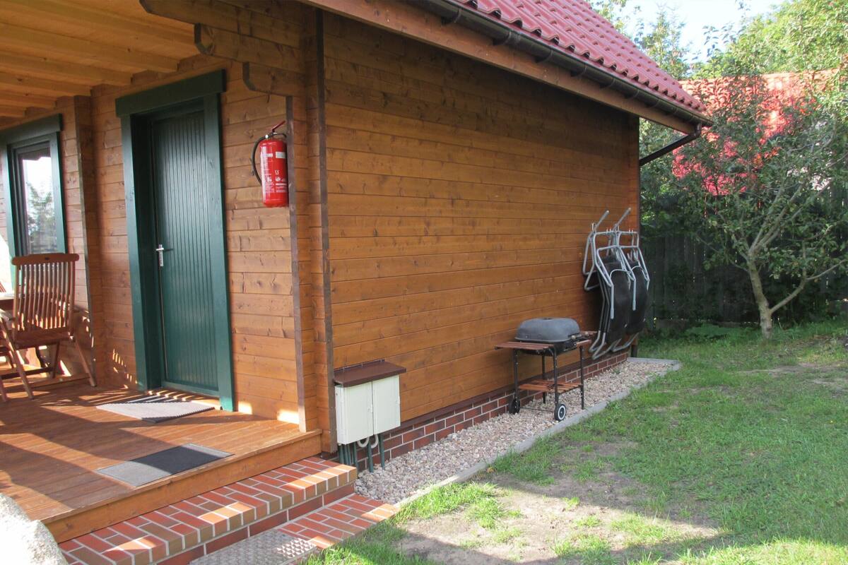 Eine Holzhütte mit grüner Tür, einem an der Wand befestigten Feuerlöscher, einem Grill draußen und einem Stuhl in der Nähe des Eingangs.