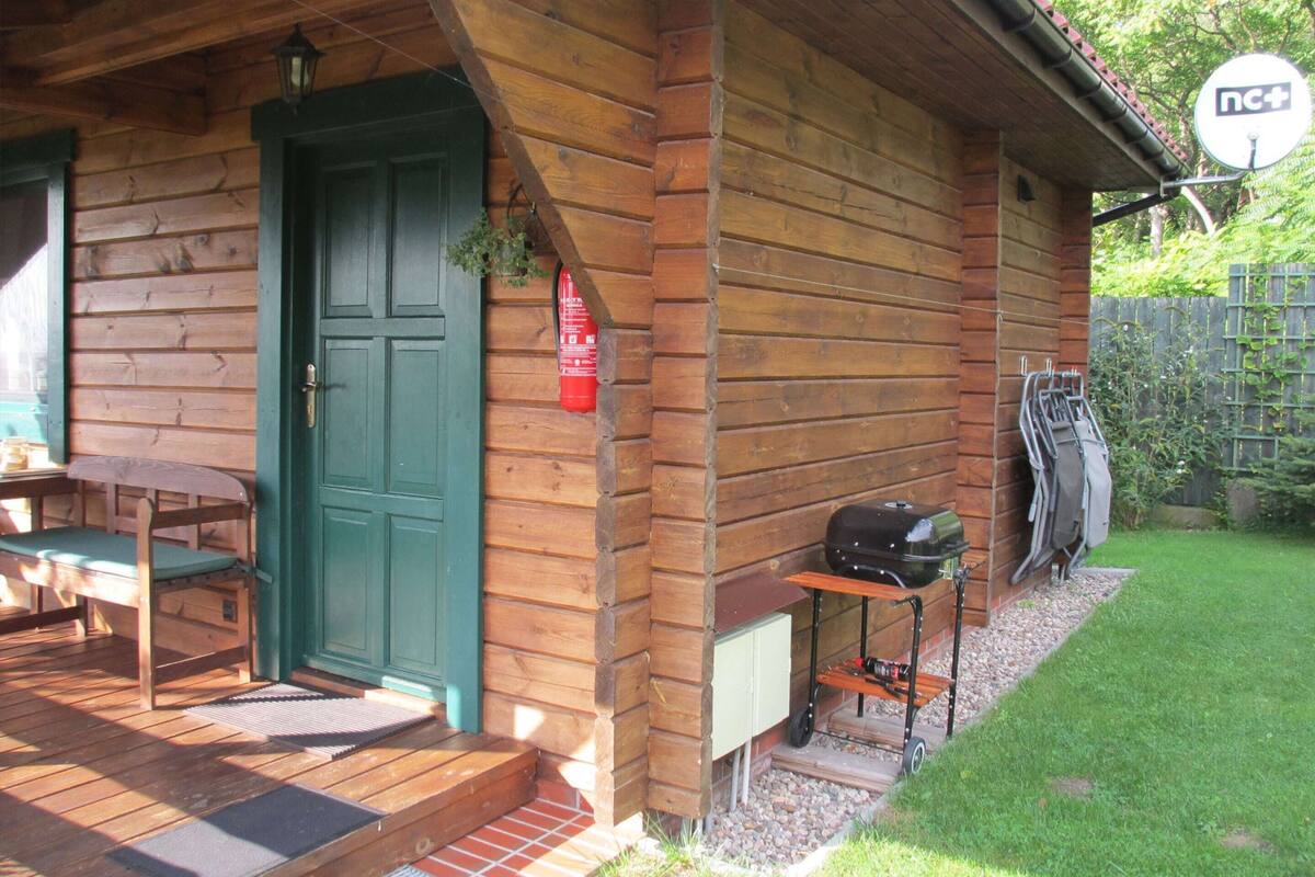 Eine Holzhütte mit einer grünen Tür, einer kleinen Veranda mit einer Bank, einem Grill und einer Satellitenschüssel.