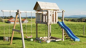Eine Holzspielkonstruktion mit Rutsche und Schaukeln in einer grünen Wiese.