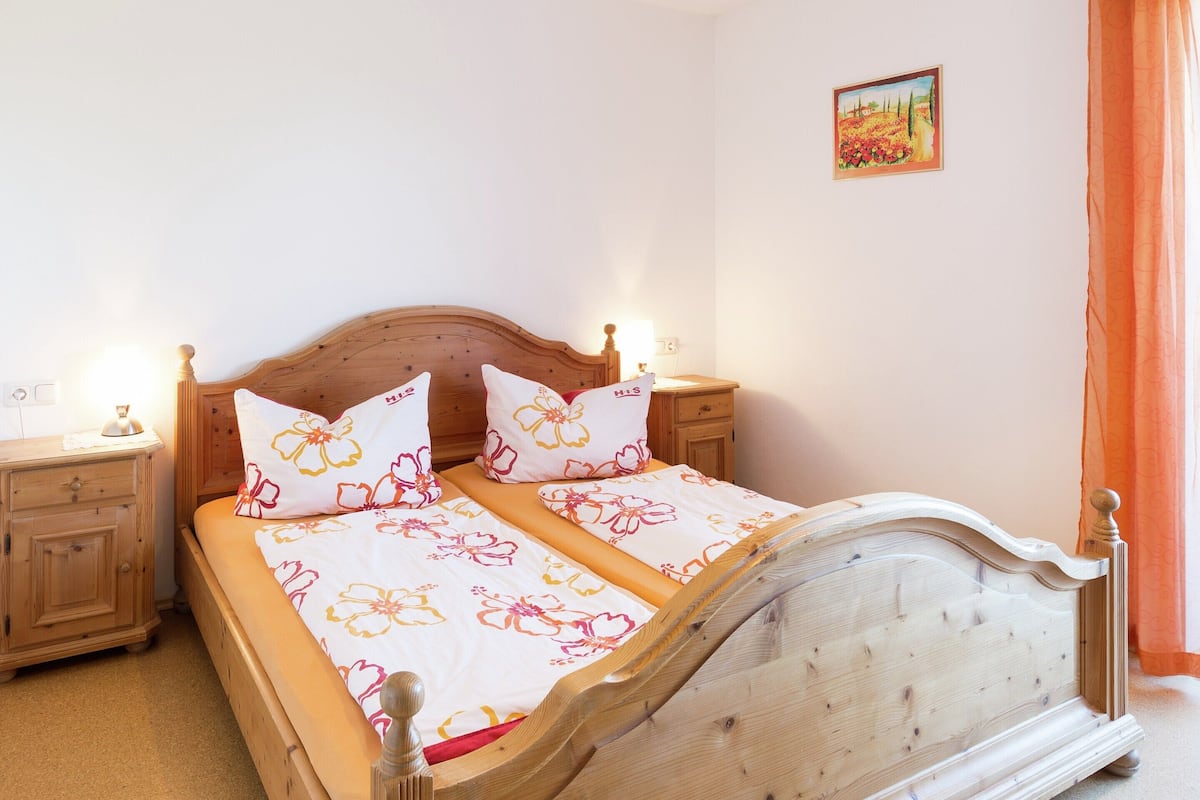Een tweepersoonsbed met bloemenbeddengoed, een houten hoofdbord, nachtkastjes met lampen en een klein schilderij aan de muur.