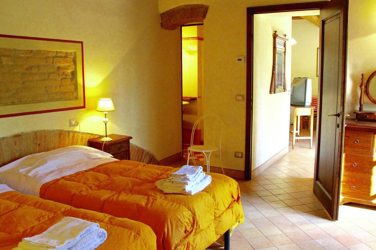 A hotel room with two beds, a desk, a chair, and a television.