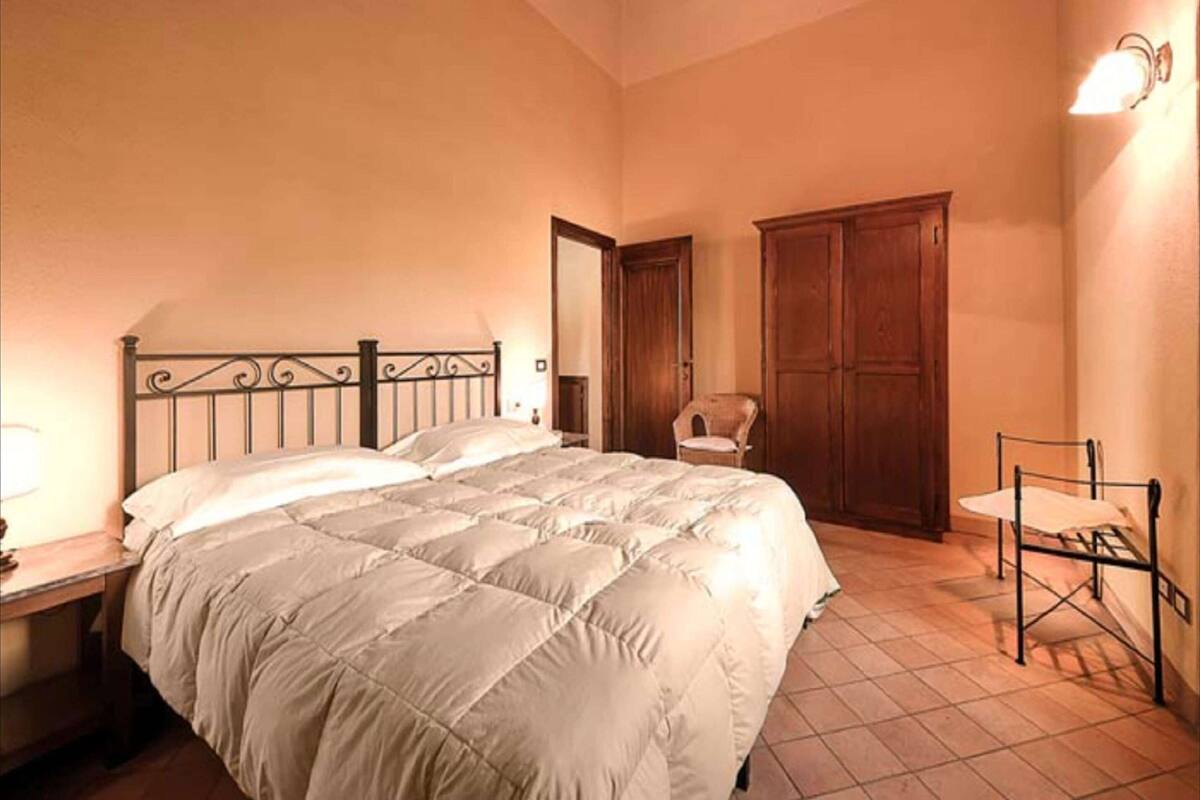 A bedroom with a large bed, a wooden wardrobe, a small table, and a chair.