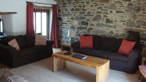 A cozy living room with two dark sofas, a wooden coffee table, and a stone wall.