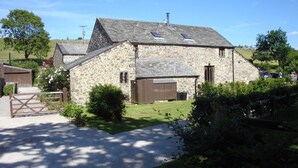 A stone farmhouse with a gravel driveway, a wooden gate, and a small garden.