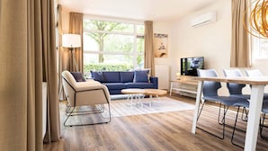 A modern living room with a sofa, armchair, coffee table, TV, and dining area. - Luxury Chalet With Dishwasher, in a Holiday Park in the Middle of De Veluwe (Ede)