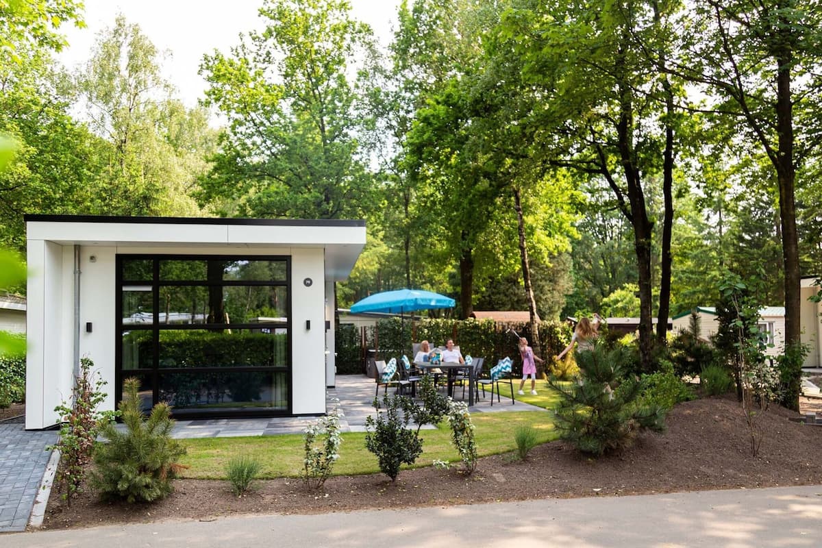 A modern outdoor seating area with a glass enclosure, surrounded by greenery and trees.