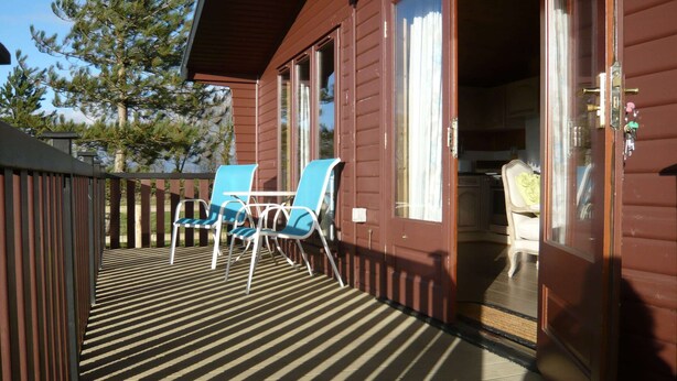 Une cabane en bois avec une terrasse, deux chaises bleues et une porte donnant sur l’intérieur.