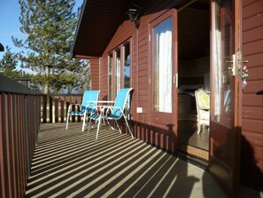 A wooden cabin with a deck, two blue chairs, and a door leading inside. - Spacious Cottage With Sauna Looking out on Astonishing Grasslands (Romney Marsh)