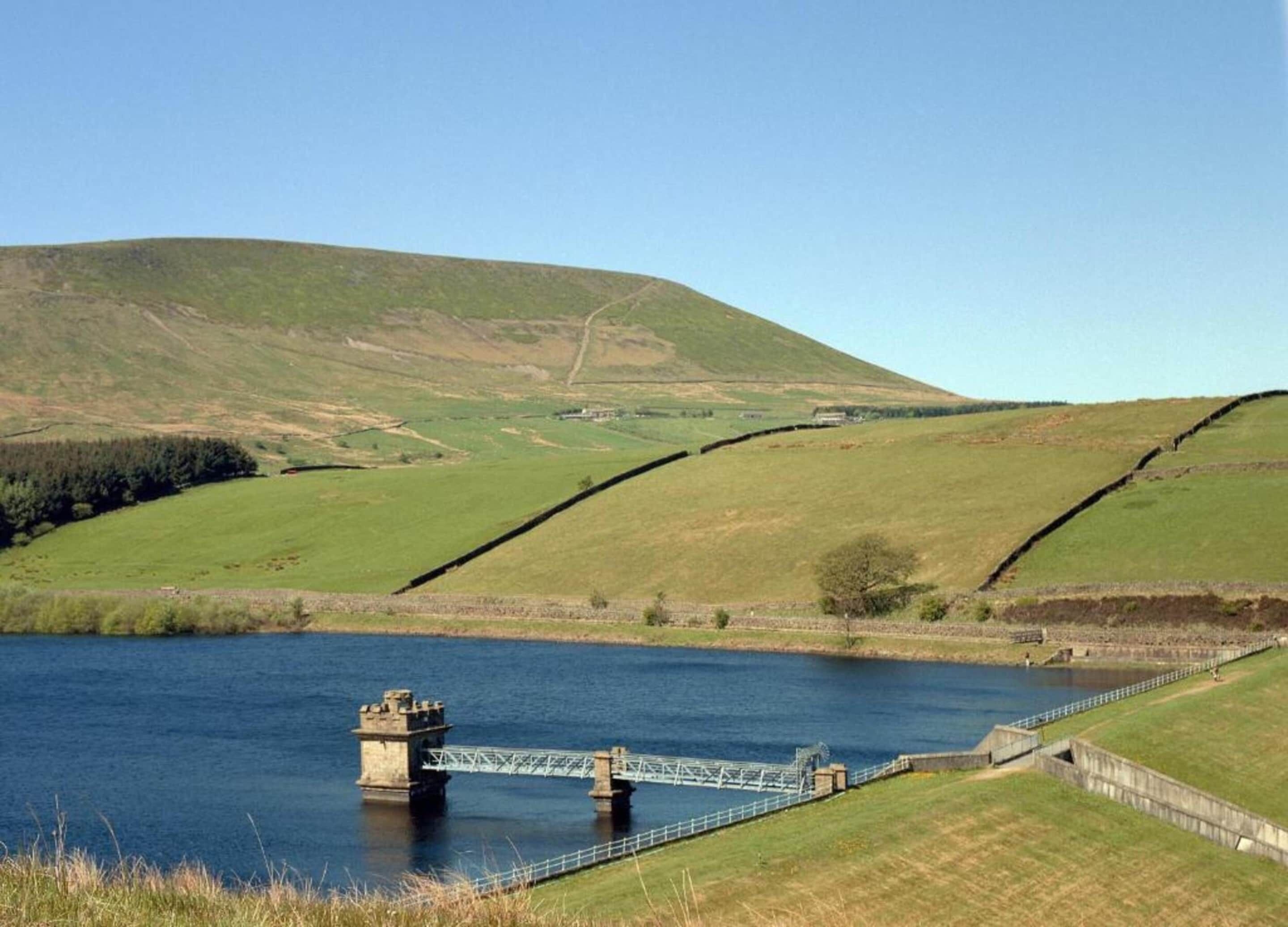 A bridge over a calm river with a hilly landscape in the background.